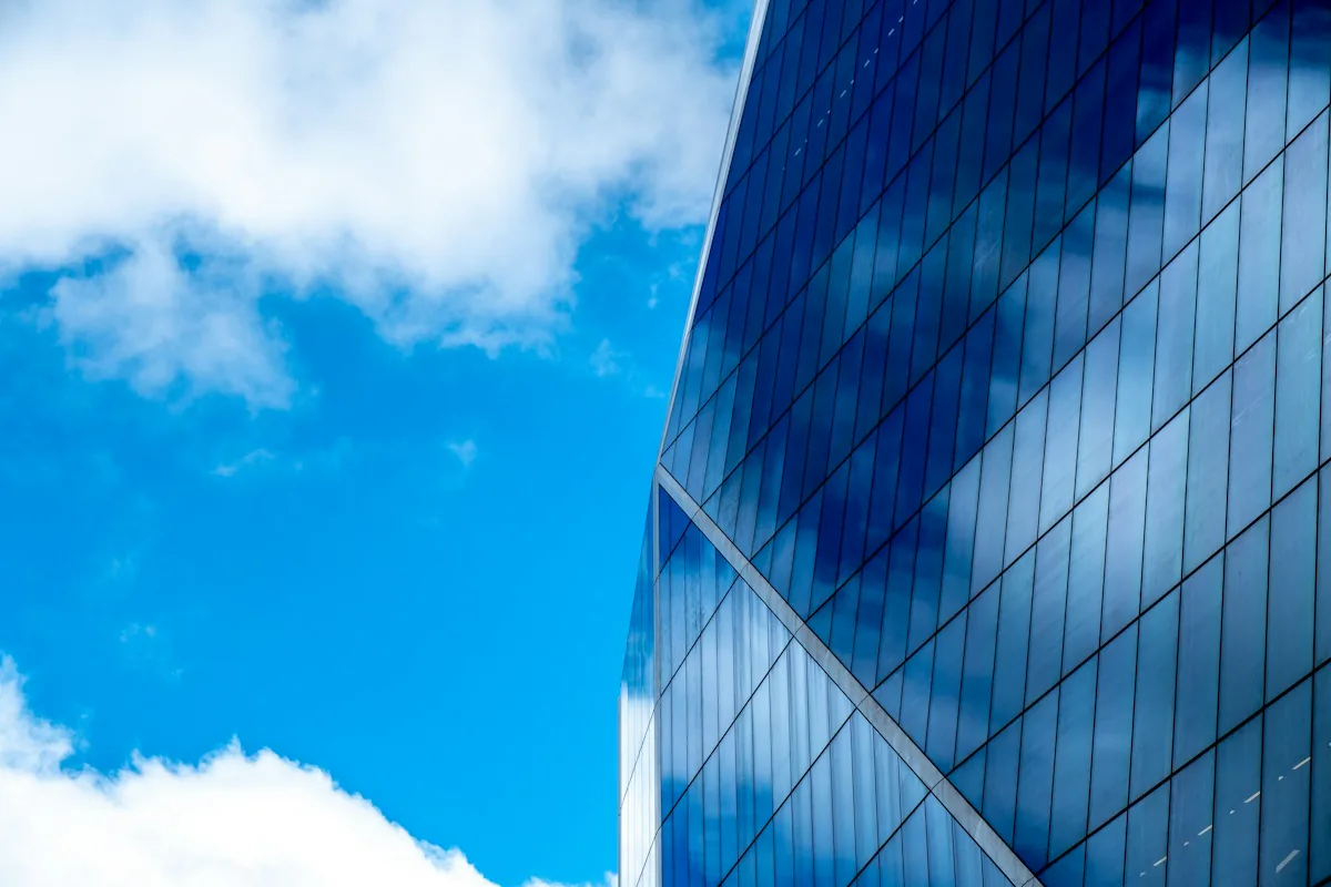 A blue glass tower reflecting clouds against a bright sky
