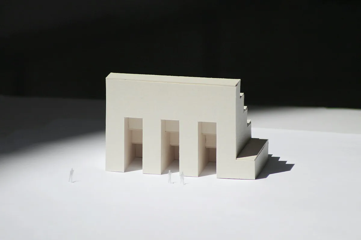 A small white card model of a building casting a soft shadow across a white table